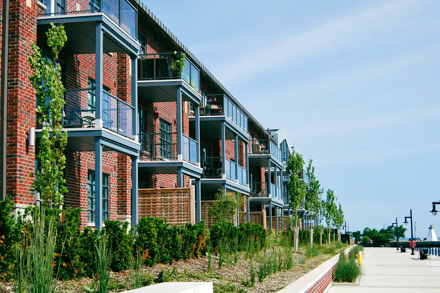 A row of red-brick apartment buildings with balconies and planted beds.