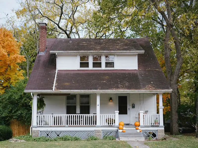 A white two-storey house with a front porch among trees.