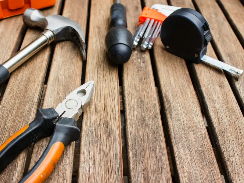 A hammer, pliers and a tape measure on a wooden workbench.