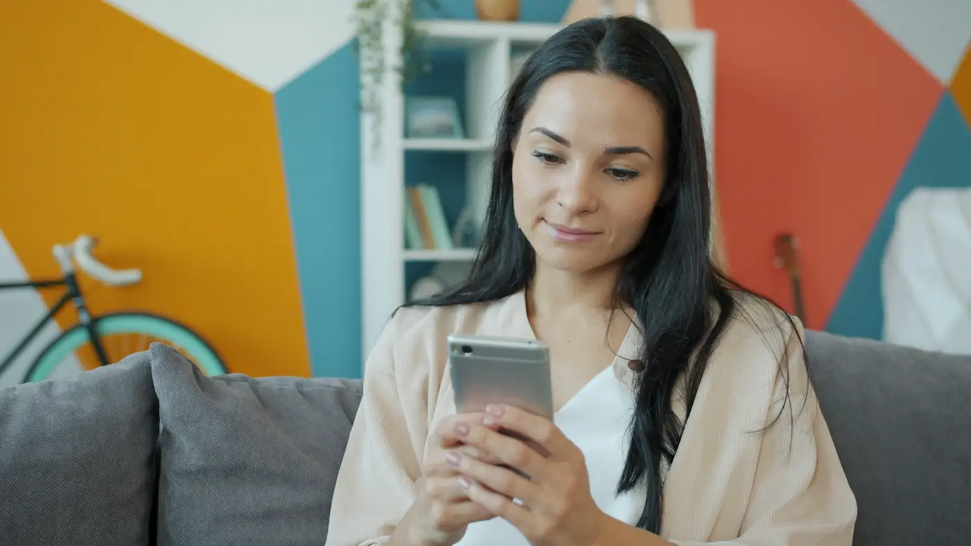 A woman on her couch at home, checking her phone.