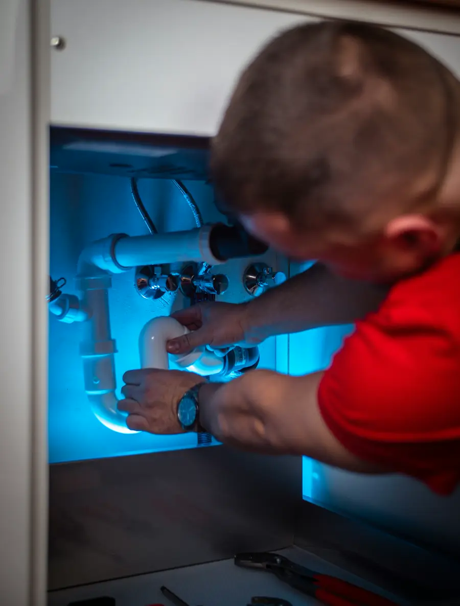 A plumber working on the pipes under a sink.